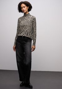Beżowa i czarna bluzka z długim rękawem i stójką w leopardzie, zestawiona z czarnymi szerokimi spodniami i botkami, na neutralnym tle.