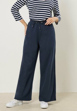 Person iført marineblå vidde bukser med snor i taljen, kombineret med hvide sneakers og en marineblå og hvidstribet langærmet top.