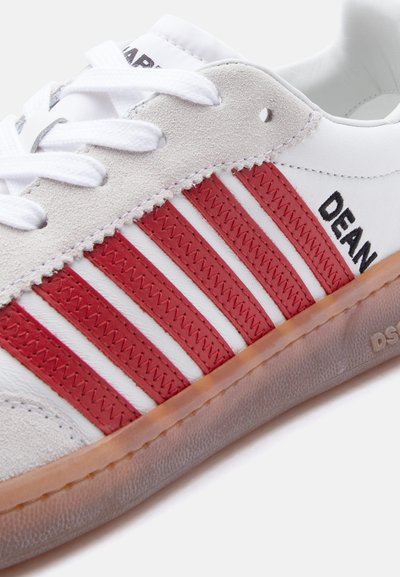 Λευκό αθλητικό παπούτσι με κόκκινες ραμμένες ρίγες, μπεζ σουέντ λεπτομέρειες, σόλα καραμέλας και το όνομα «DEAN» κεντημένο κοντά στη φτέρνα στη πλευρά.