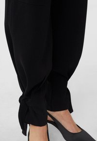 Czarne zwężane spodnie z miękkiego materiału, z wiązanymi mankietami. Połączone z eleganckimi czarnymi szpilkami, podkreślającymi smukłą sylwetkę.