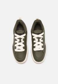 Scarpe sportive in pelle verde con lacci bianchi e suola color crema. Presentano un collare imbottito e un logo prominente sulla linguetta.