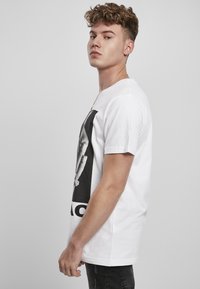 White cotton t-shirt with a large black graphic print on the front, short sleeves, and a round neckline; model stands sideways.