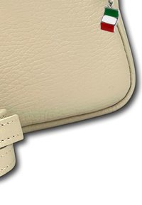 Crème-kleurige leren handtas met een gestructureerd oppervlak, voorzien van een kleine metalen Italiaanse vlag charme die aan de ritssluiting is bevestigd.
