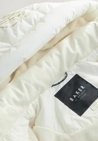 Hvid polstret jakke med blødt fleecefor, sort "Bakery by Ted Baker London" label på indersiden af kraven.