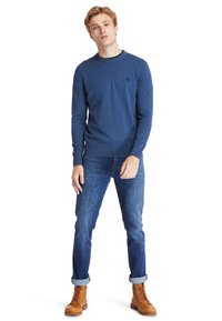 Maglione blu navy lavorato a maglia con scollo rotondo e polsini a coste, abbinato a jeans in denim arrotolati e stivali marroni con lacci.