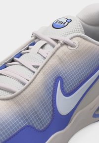 Κοντινό πλάνο λευκού και μωβ αθλητικού παπουτσιού Nike Air Max με γλώσσα από δίχτυ, κορδόνια και ορατά λογότυπα της μάρκας στη γλώσσα και στο πλάι.