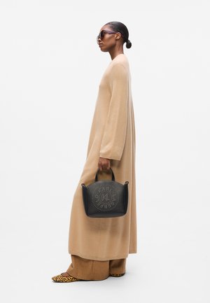 Beige long-sleeve dress with wide sleeves, paired with terracotta pants. Black handbag with studded logo, animal print shoes.