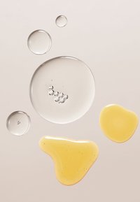 Des gouttes de gel translucides de tailles variées dans des teintes claires et jaunes, présentant des bulles et des textures lisses sur un doux fond beige.
