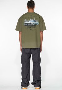 Olivenfarvet t-shirt med rygprint af en vintage bil og bylandskab, parret med mørke cargo-bukser med flere lommer og elastiske manchetter.