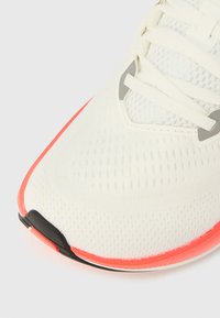 Scarpa da ginnastica bianca con tomaia in mesh, lacci bianchi e bordo suola arancione acceso, mostrata in primo piano su sfondo neutro.