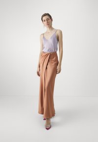 Camisola di raso viola chiaro con spalline sottili abbinata a una gonna maxi drappeggiata di colore arancione. Le calzature presentano dettagli rosa e trasparenti.