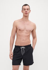 Pantaloni da bagno neri con vita regolabile tramite cordino, realizzati in un tessuto leggero e ad asciugatura rapida, e con un piccolo dettaglio del logo.