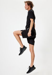Sort atletisk t-shirt og shorts med et elegant design. Sættet er parret med sorte snørebånds atletik sko med teksturerede såler.