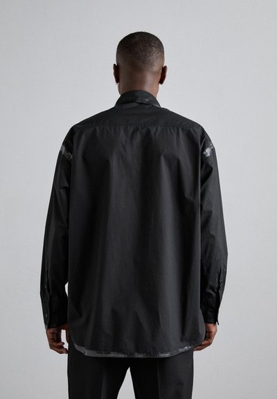 Sort langærmet skjorte med en glat tekstur, der har en lige kant, knapmanchetter og subtile designaccenter på skuldrene.