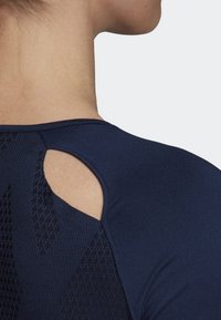 Marinblå atletisk topp med en texturerad design, utskärning bak och en figurnära siluett. Mjukt material med en nära kroppskänsla.