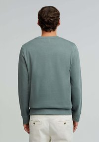 Zielony sweter wykonany z lekkiego materiału, z okrągłym dekoltem i ściągaczami przy mankietach. Prosty design bez widocznych wzorów czy zdobień.