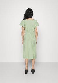 Kukkakuvioinen vihreä midimekko, jossa on lyhyet puffihihat, joustava vyötärö ja soljuva kangas. Yhdistetty mustien paljettikorokepohjaisten kenkien kanssa.