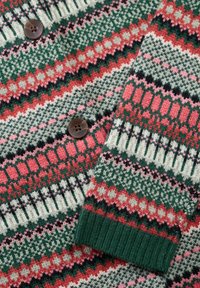 Gebreide trui met multicolor geometrische patronen in groen, rood, roze en wit, voorzien van twee bruine knopen en een geribbelde mouw.