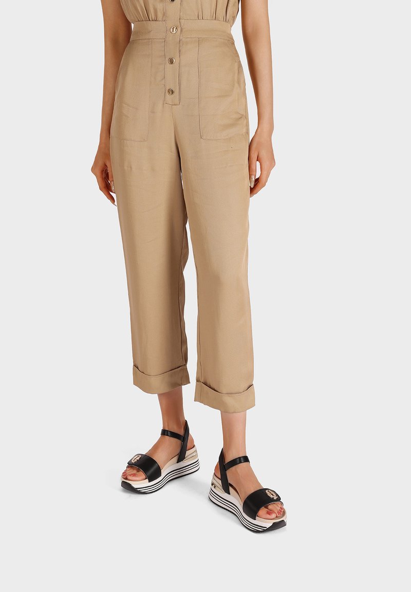 Pantaloni beige cropped con tasche anteriori e orli arrotolati, abbinati a sandali con zeppa bianco e nero con cinturino e dettaglio del logo.