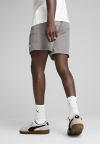Grå shorts med en glat tekstur og sidelommer, parret med hvide PUMA sneakers med sorte accenter og beige detaljer. Hvide sokker synlige.