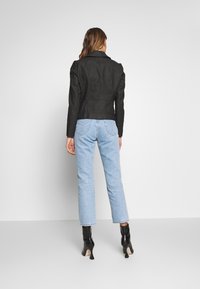 Musta tekonahkavuori takki, jossa on jämäkät olkapäät ja kauluskankaat, yhdistettynä vaaleansiinisiin suoriin farkkuihin ja mustiin korkokenkällisiin nilkkasaappaisiin.