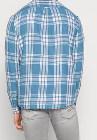 Niebieska koszula w kratę z kołnierzykiem na guziki, z paskami w jasnoróżowym i białym kolorze. Długie rękawy z regulowanymi mankietami. Miękka tekstura tkaniny.