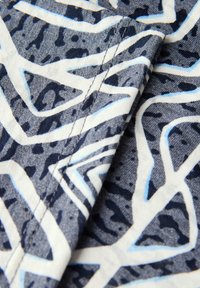 Tessuto di cotone con un motivo geometrico nei colori blu navy, bianco e azzurro chiaro, con cuciture visibili e variazioni di texture.