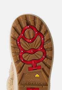 Sålen på en støvle med et hævet, tekstureret mønster i lys brun, med et rødt træksystem og fem sølvfarvede pigge for greb.