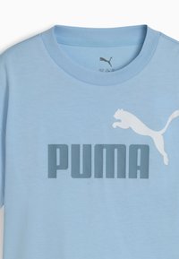 Gaiši zila kokvilnas t-krekls ar lielu pelēku "PUMA" logo un baltu lecoša puma attēlu. Klasiska apaļā kakla dizains, īsas piedurknes.