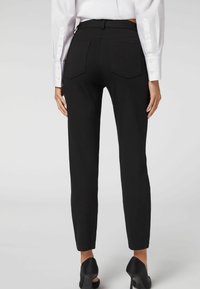 Pantalones negros ajustados con una textura suave, cintura alta y dos bolsillos traseros. Combinados con una camisa blanca de manga larga y tacones negros.