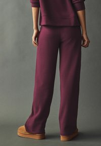 Bordo sweatpants opuštenog kroja sa mekim materijalom, širokim nogavicama i pripremom od pamuka, upareni s laganim smeškim antilop cipelama na slip-on.