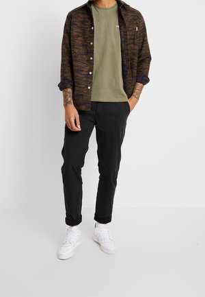 Braun und marineblau gemustertes Hemd, olivgrünes T-Shirt, schwarze Hose und weiße Sneakers. Material besteht aus Baumwollmischungen; lässige Passform.