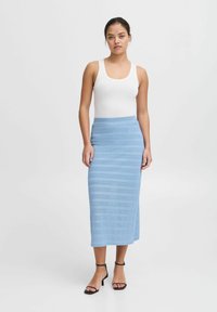 Fustă tricotată ribbed de culoare albastru deschis, cu o siluetă dreaptă, asortată cu un top alb fără mâneci și sandale negre cu bretele, pe un fundal simplu.