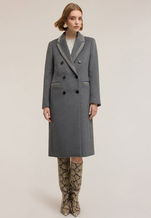 Grå ull dubbelknäppt kappa med kontrasterande krage, sex svarta knappar och en lång siluett. Kombinerad med knähöga stövlar med ormskinnsprint.