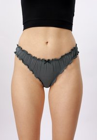 Donna che indossa biancheria intima stile bikini grigio scuro con volant e top corto nero, mostrata dalla vita alla parte superiore delle cosce.