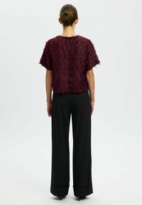 Top bordeaux con texture e maniche corte abbinato a pantaloni neri a gamba larga a vita alta, caratterizzati da una silhouette elegante e sartoriale.