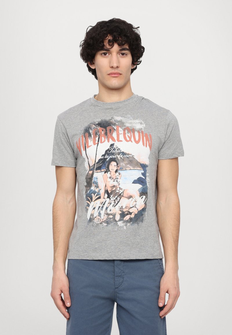 Camiseta de algodón gris con un colorido estampado gráfico de una figura en una playa, con el texto "VILEBREQUIN" en rojo en la parte superior. Manga corta, cuello redondo.