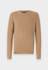 Pull en tricot beige avec un motif texturé, col rond et poignets côtelés. Petit logo sur la poitrine.