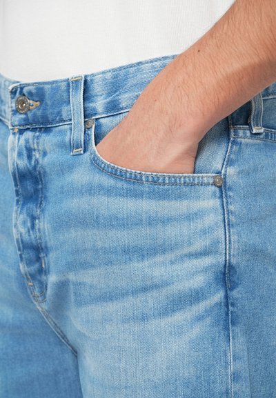 Heledad sinine teksapüksid, millel on kulumistunne, keskmise tõusuga vöökoht, nööp sulgemine ning esikott, millel on peen õmblustegu.