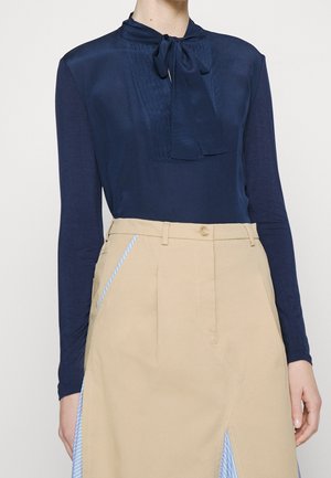 Blusa de manga larga azul marino con un cuello atado, que presenta un panel frontal texturizado, combinada con falda de talle alto beige con detalles a rayas.