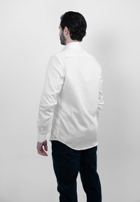 Witte long-sleeve shirt met een gladde textuur, rug yoke en een gebogen zoom, gecombineerd met donkere broek. Schoon, minimalistisch ontwerp.