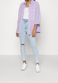 Chemise boutonnée lavande, débardeur blanc à côtes, jeans skinny déchirés bleu clair, et baskets blanches au design minimal.