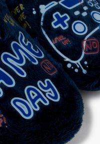 Tmavě modré plyšové pantofle s herními motivy, včetně ovladačů a textu jako "LEVEL UP!" a "GAME DAY," v kontrastních barvách.