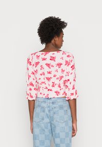 Blusa curta com base branca e padrão floral rosa, apresentando punhos elásticos e cintura franzida; combinada com jeans xadrez azul claro.