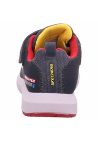Scarpa da atletica grigia scura con collare imbottito giallo, dettagli rossi e suola intermedia bianca. Presenta un'etichetta impermeabile sul lato.