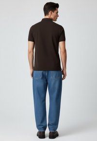 Braunes Poloshirt und blaue Jeans, getragen von einer Person, Rückansicht. Die Jeans haben ein strukturiertes Muster und Gesäßtaschen.