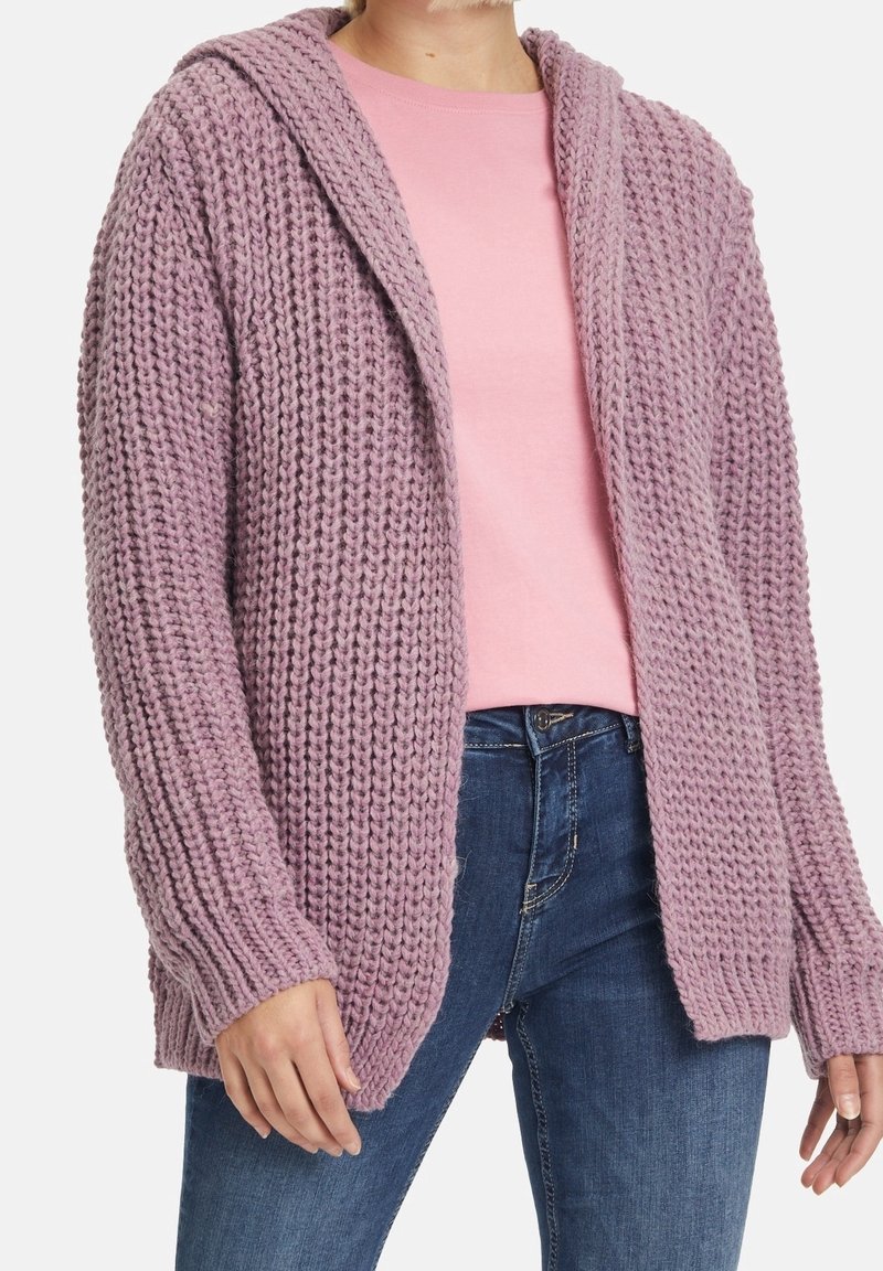 Cardigan tricoté lavande avec points texturés, ouverture devant et capuche. Porté par-dessus une chemise rose et associé à un jean bleu.