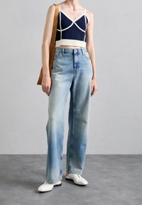 Top corto navy con ribete marfil, jeans de tiro alto en azul claro y zapatillas blancas sin cordones. La modelo también lleva un bolso de hombro beige.