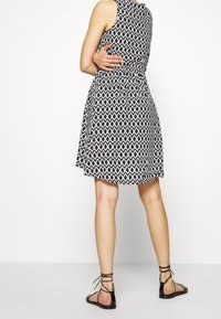 Robe à motifs noir et blanc avec un corsage ajusté, une jupe évasée et sans manches ; associée à des sandales noires à lanières.