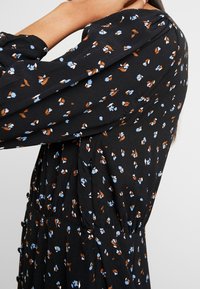 Robe fleurie noire avec des motifs floraux bleus et bruns, dotée de manches longues et d'une taille froncée avec de petits boutons sur le devant.